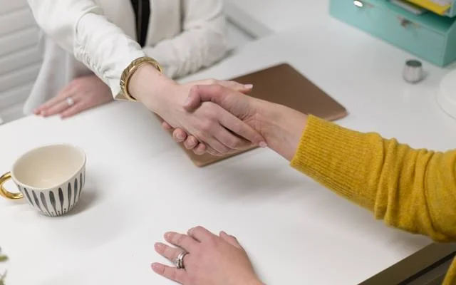 Two people shaking hands across a desk